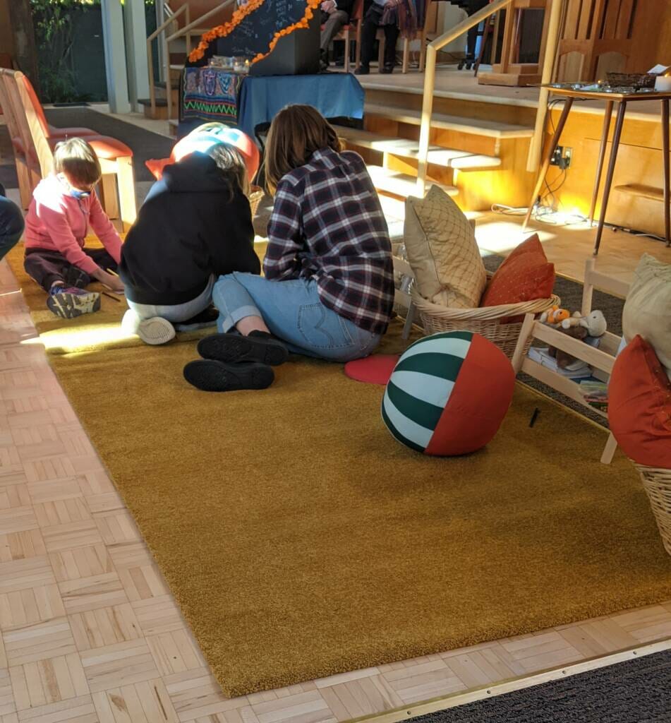 child and teens on carpet at front of sanctuary, drawing and colouring. Open space and pillows in foreground