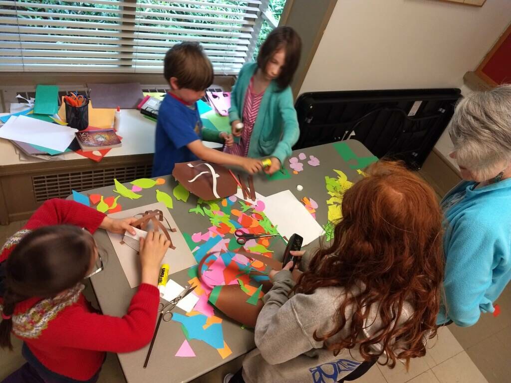 children gathered around a table creating with many colourful pieces of paper.